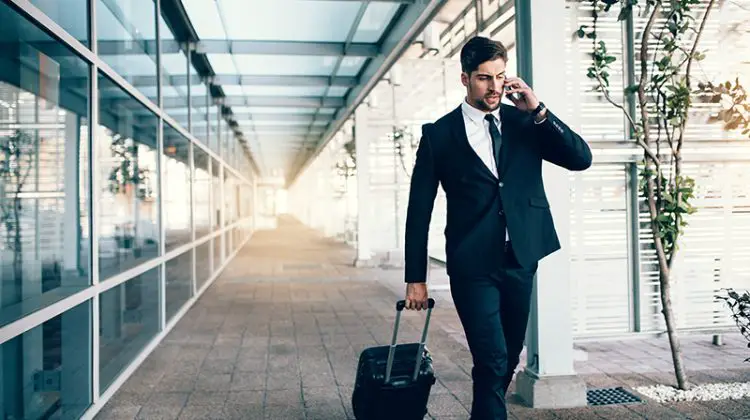 Handsome young man on business trip walking with his luggage and talking on cellphone at airport