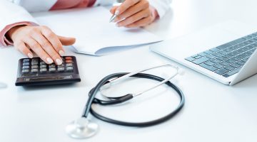 Doctor using calculator writing bills and doing bookkeeping