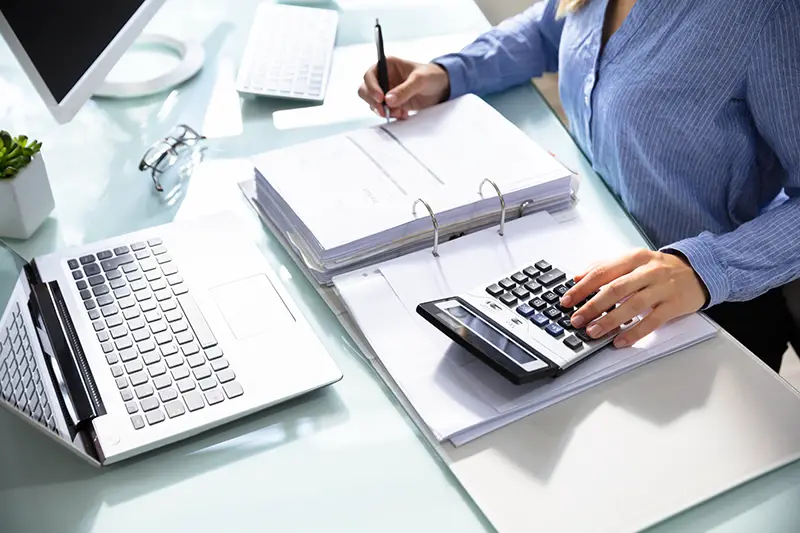 Businesswoman's Hand Calculating Bill With Calculator Over Desk In Office
