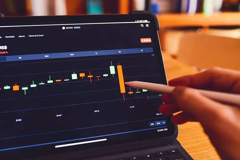 Person pointing a pen on trading graph on laptop screen