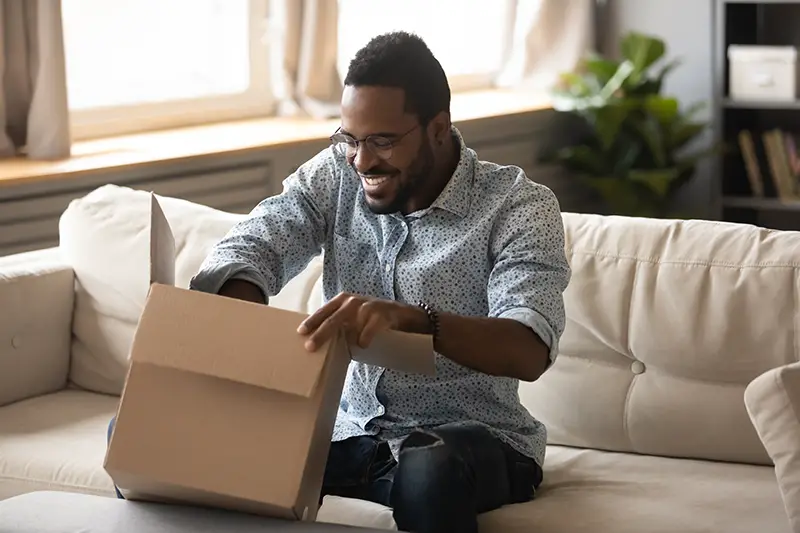 happy ethnic male consumer unpack parcel receive retail purchase 