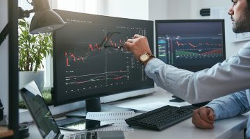 Young trader is pointing at graphs on computer screen and analyzing data