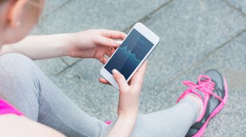 Athletic lady in uniform and sneakers use smartphone to check activity on screen during rest