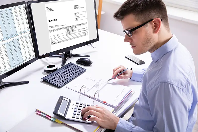 Side View Of Businessman's Hand Calculating Invoice At Workplace