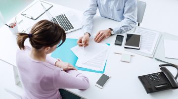 Advisor meeting with a customer in his office, he is explaining a contract document and policy to the woman sitting at his desk