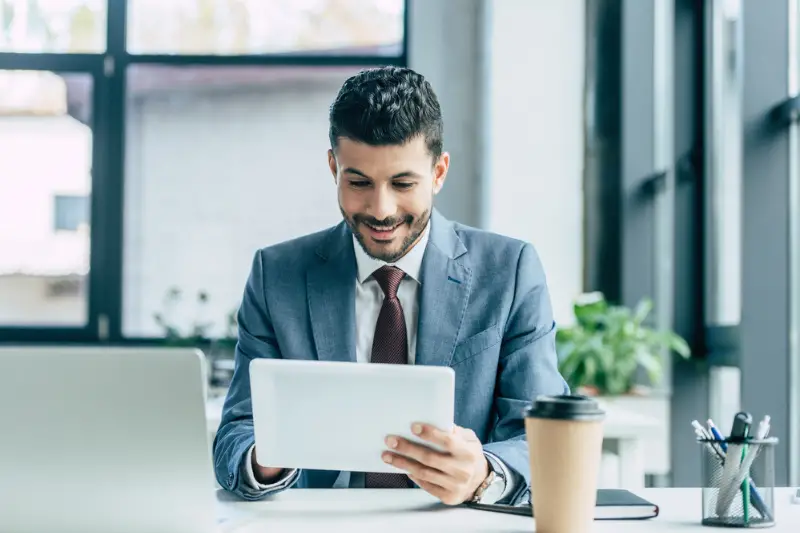 Cheerful businessman using digital tablet while sitting in his office desk