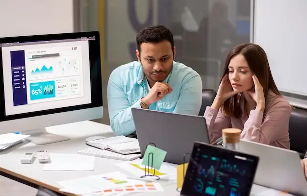 Man and woman colleagues staring in computer at office desk