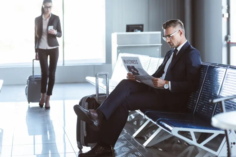 Traveller sitting with luggage in airport lounge reading newspaper