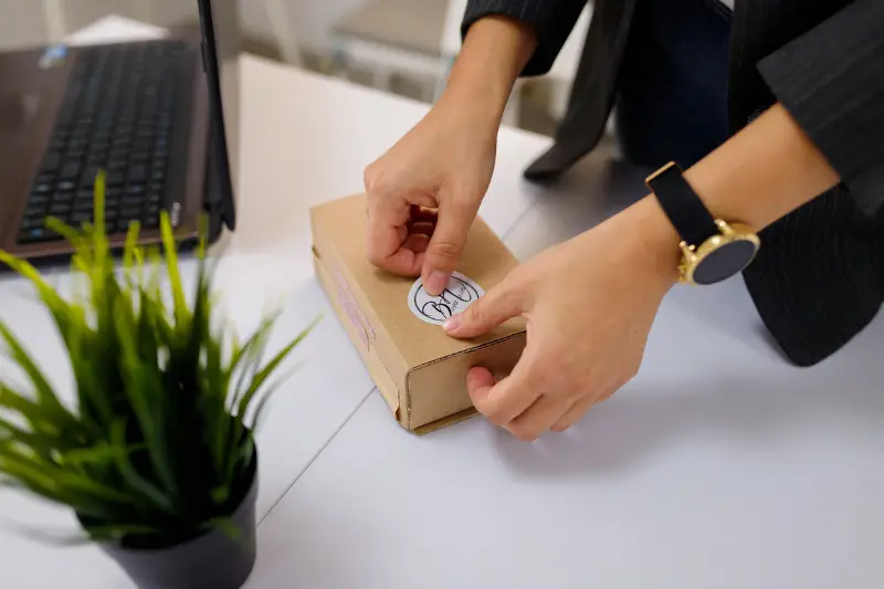 Female hands sticking a logo label on carton, paper box.