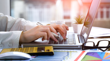Woman working using laptop beside yellow calculator