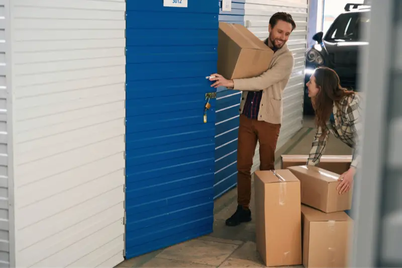 Young man and woman with big cardboard boxes in self storage unit