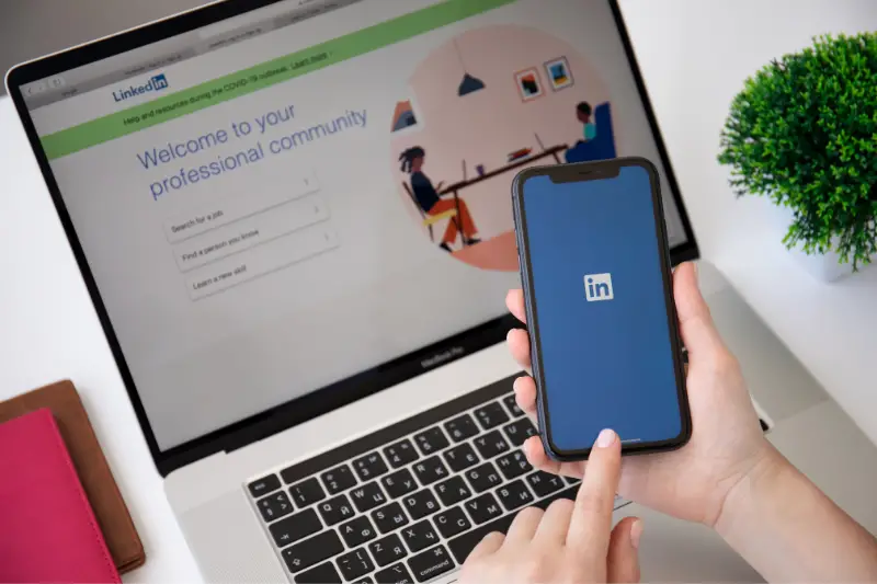 Woman hand holding iPhone 11 Macbook Pro 16 app LinkedIn