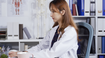 portrait asian female doctor sitting in the office is looking up information on her computer and transcribing on notebook with pen.
