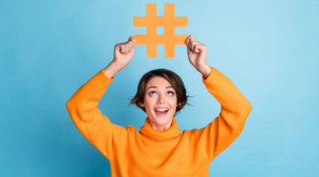 Portrait of cheerful astonished person look hands hold paper hashtag symbol isolated on blue color background