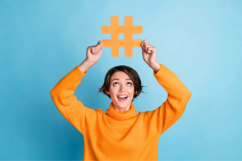 Portrait of cheerful astonished person look hands hold paper hashtag symbol isolated on blue color background