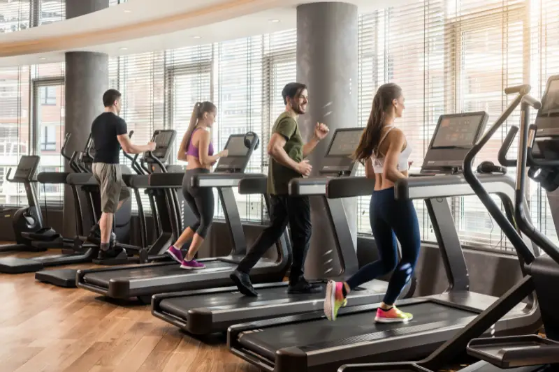 Group of four people, men and women, running on treadmills in modern and luminous fitness gym