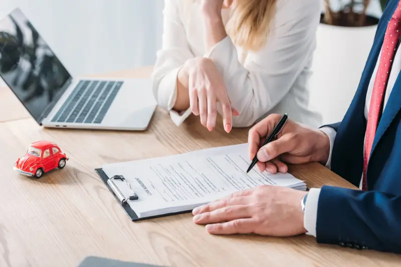 Cropped shot of man signing loan agreement in car dealer office