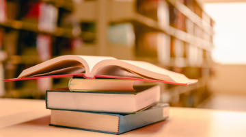 Opened book with stack of books on the desk wood in the library.