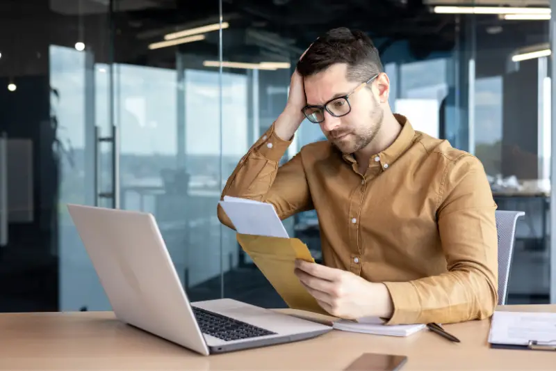 A worried young man, a businessman, an accountant works in the office, received a letter with accounts, credit, debt, a notice of bankruptcy