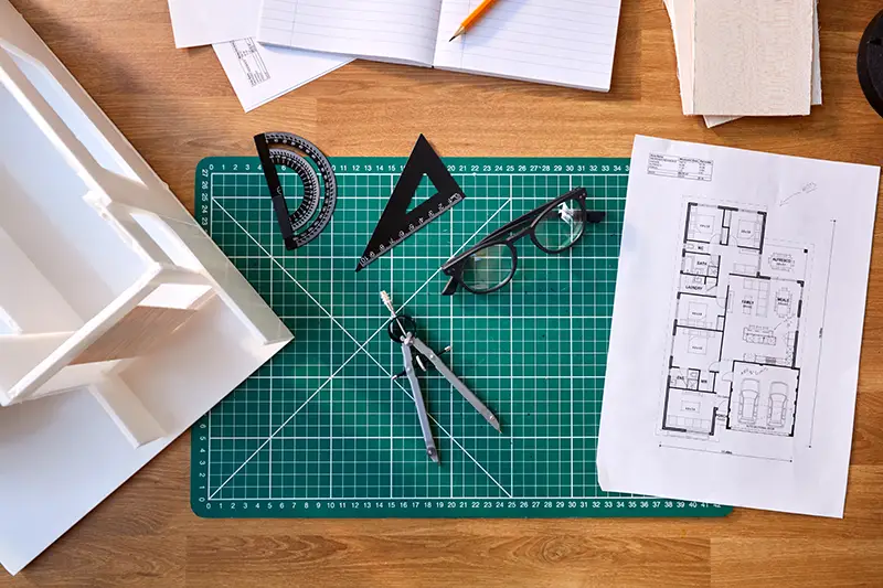 Overhead Shot Of Desk In Architects Office With Plans Drawing Instruments And Model