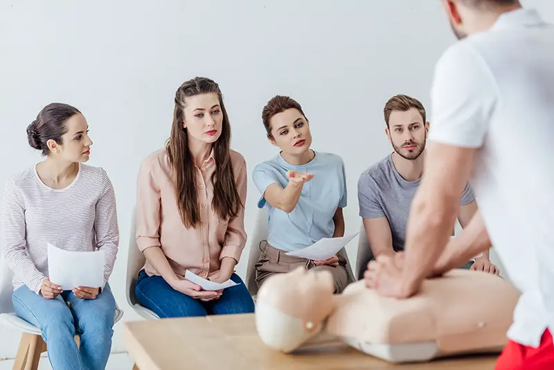 back view of instructor performing cpr on dummy during first aid training with group of people