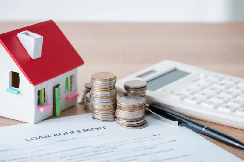 House model, silver and golden coins, loan agreement and calculator on wooden surface