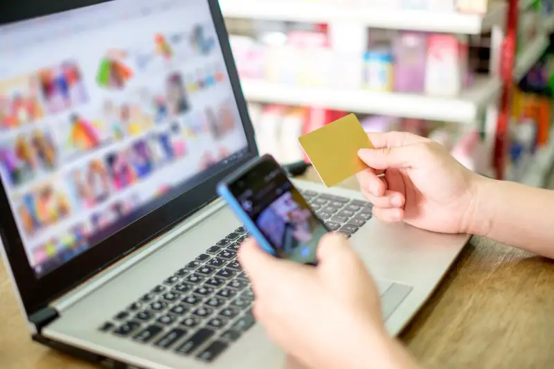Hand holding credit card and using laptop with smartphone for payment shopping online