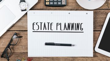 Estate Planning text on note pad, office desk with electronic devices, computer and paper, wood table from above, concept image for blog title or header image.