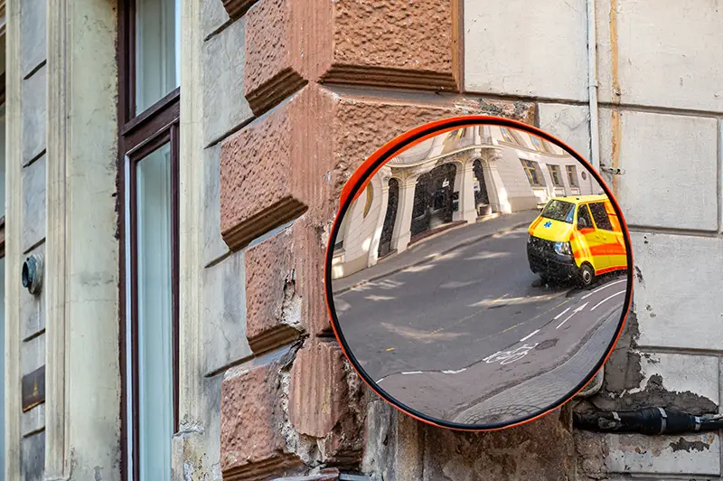 a traffic mirror with a yellow ambulance emergency car parked on the side of the street