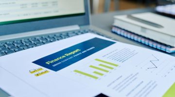 Financial papers with statistics and profit information on laptop keyboard