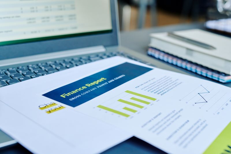 Financial papers with statistics and profit information on laptop keyboard