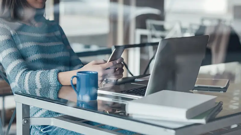 Businesswoman working at office desk and texting with her mobile phone