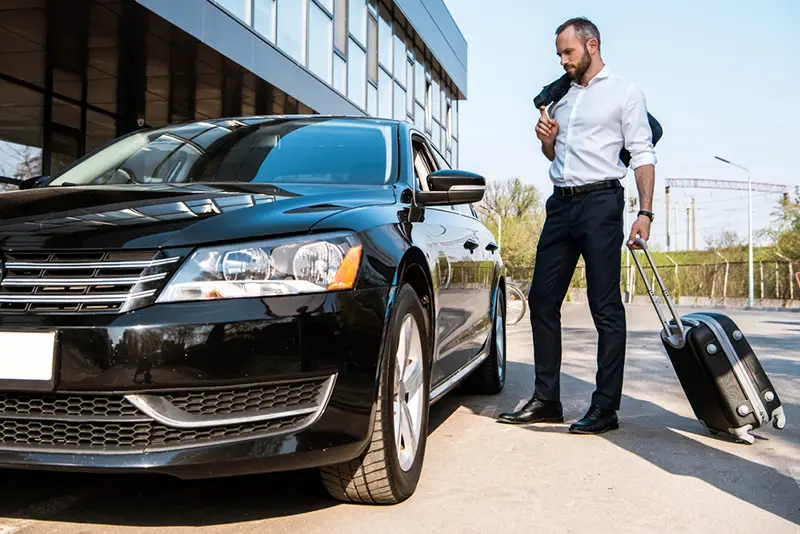 Low angle view of handsome businessman standing near black car with luggage