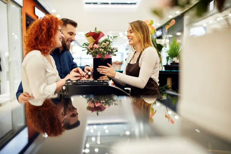Happy couple and shop assistant with potted plant at counter in flower shop