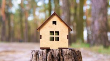 Close-up of a wooden toy house model placed on a tree stump in the forest