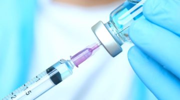 Doctor's hand holds a syringe and a blue vaccine bottle
