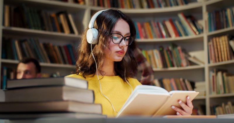 Young female student listening musc with headset inside the library