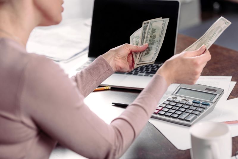 Cropped shot of woman counting money at table with laptop