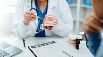 Dentist sitting at table with jaw samples tooth model in dental office