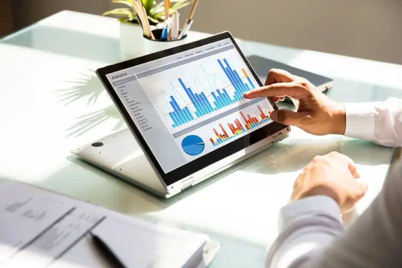 Close-up of a businessman's hand analyzing graph on laptop on workplace