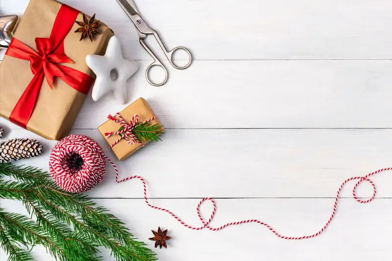 Preparing for the holidays, wrapping gifts, top view with copy space. Background with gift boxes in craft paper, striped rope, festive cookies and a branch of a Christmas tree on a table