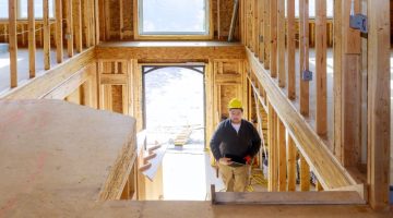 New construction house builder in hard hat walking up the stairs holding tablet PC