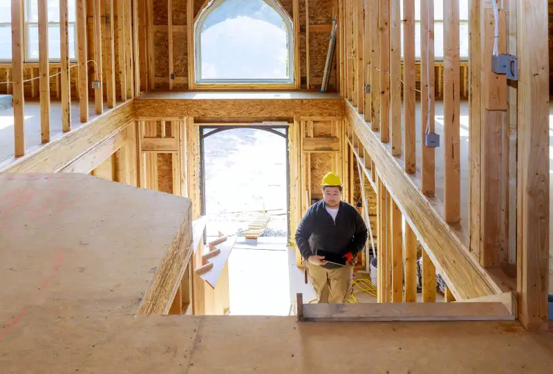 New construction house builder in hard hat walking up the stairs holding tablet PC