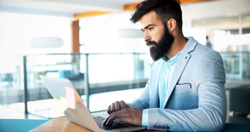 Professional handsome businessman using laptop at workplace looking at homepage of a website