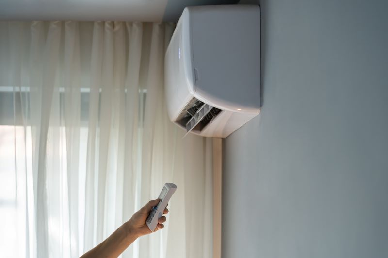 A person with a remote control turns on the air conditioner to adjust the room's temperature.