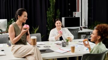 Elegant businesswomen enjoy a casual meeting in a modern office space with coffee and donuts