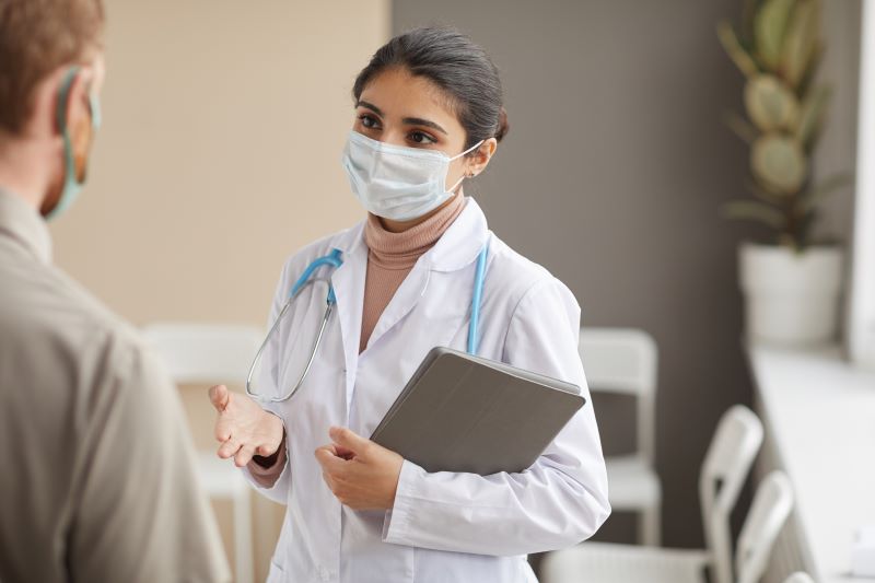 Young female doctor in protective mask talking to a patient