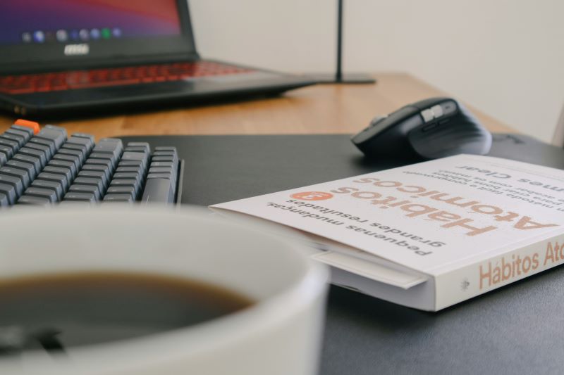 Atomic Habits by James Clear on desk next to keyboard mouse and laptop