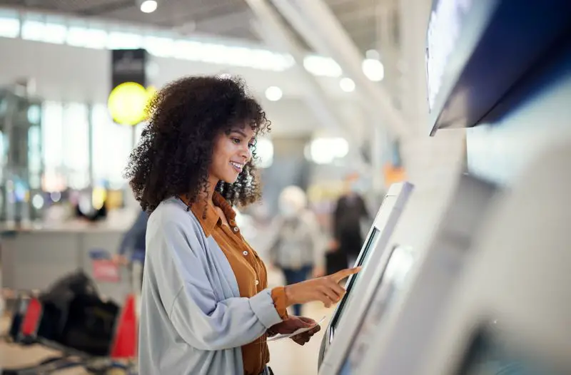 Black woman, airport and smile by self service station for ticket, registration or boarding pass.