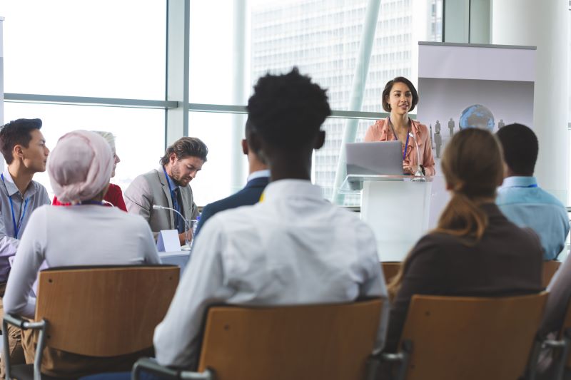 Female speaker with laptop speaking in business seminar in office building